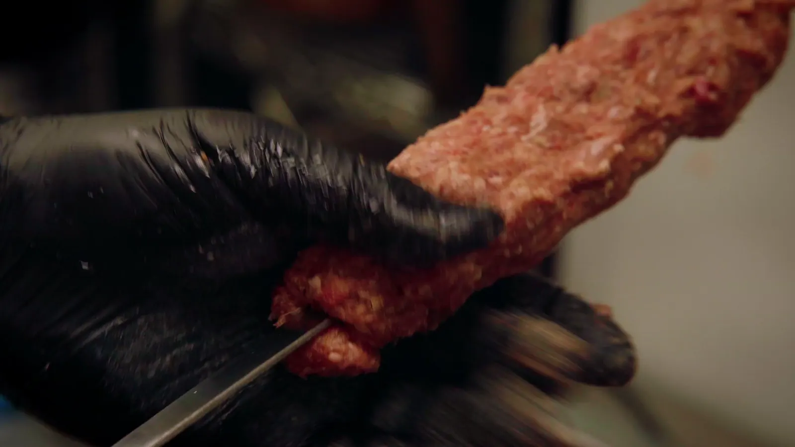 Adana kebab shaped by hand onto a wide skewer
